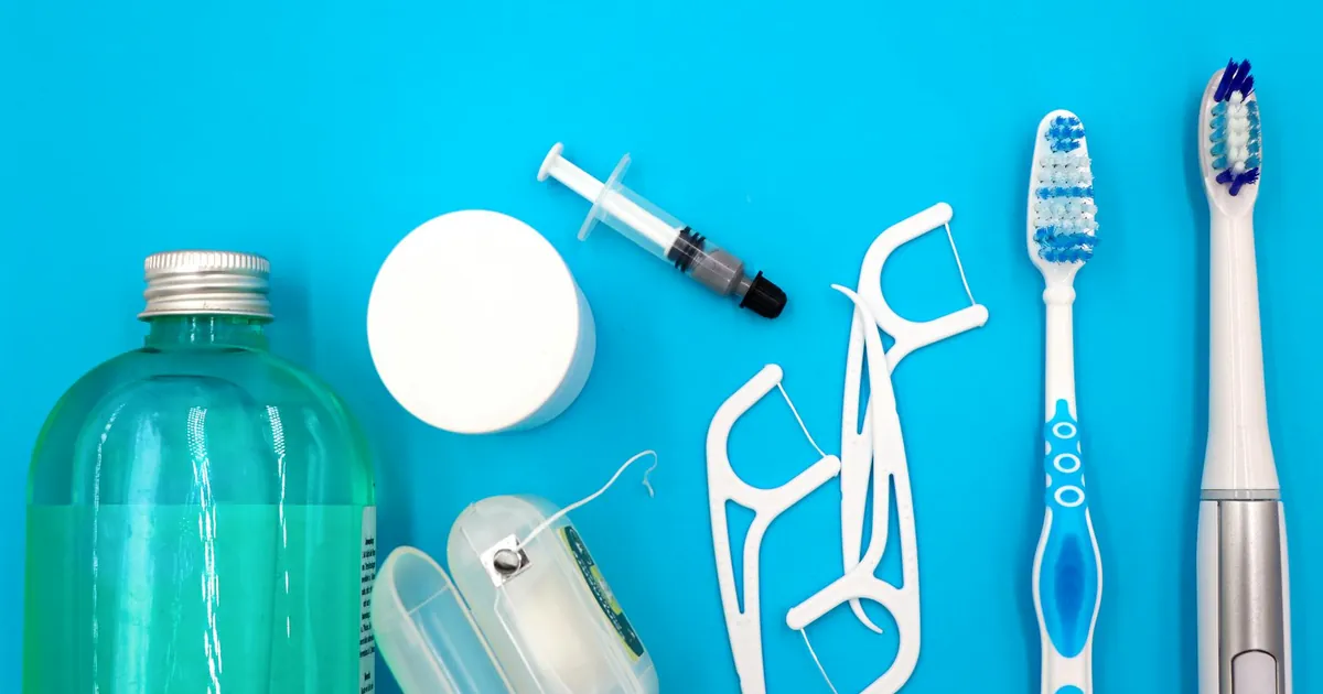 Flat lay of oral hygiene essentials including toothbrushes, floss, and mouthwash on a blue surface.