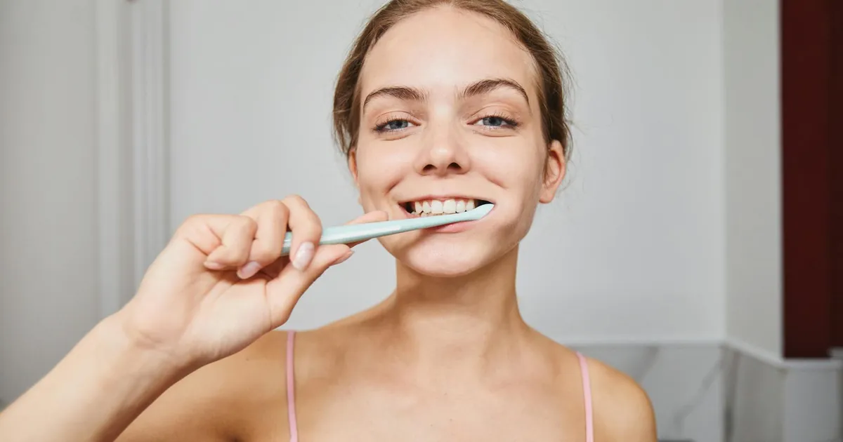 Close-up of a woman smiling while brushing teeth in a modern bathroom.