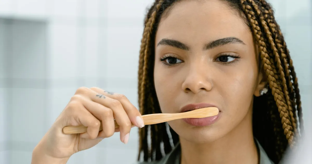 Close-up of a woman with braided hair brushing her teeth, highlighting oral hygiene.