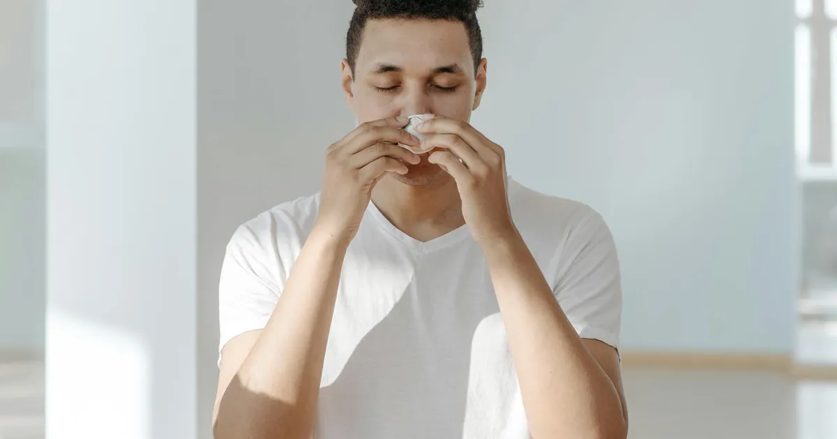 A man sneezing into a tissue, illustrating symptoms of flu or allergies.