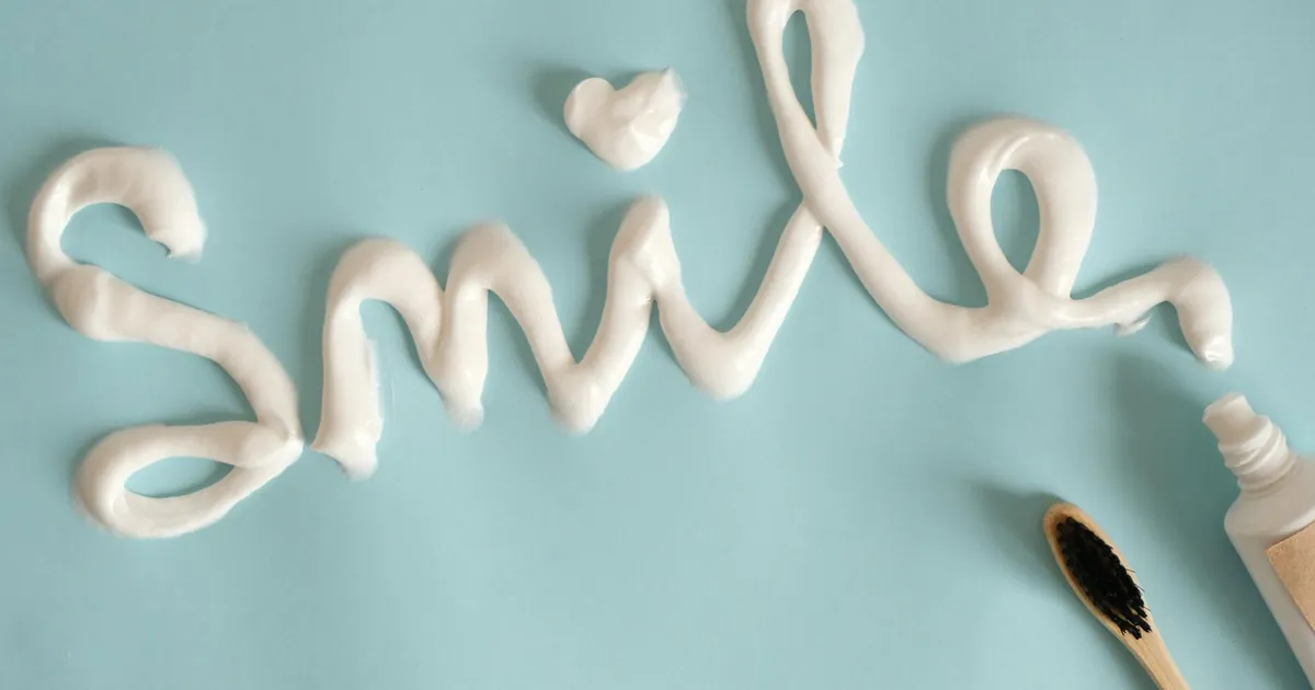 Toothpaste spelling 'Smile' on turquoise surface with toothbrush.