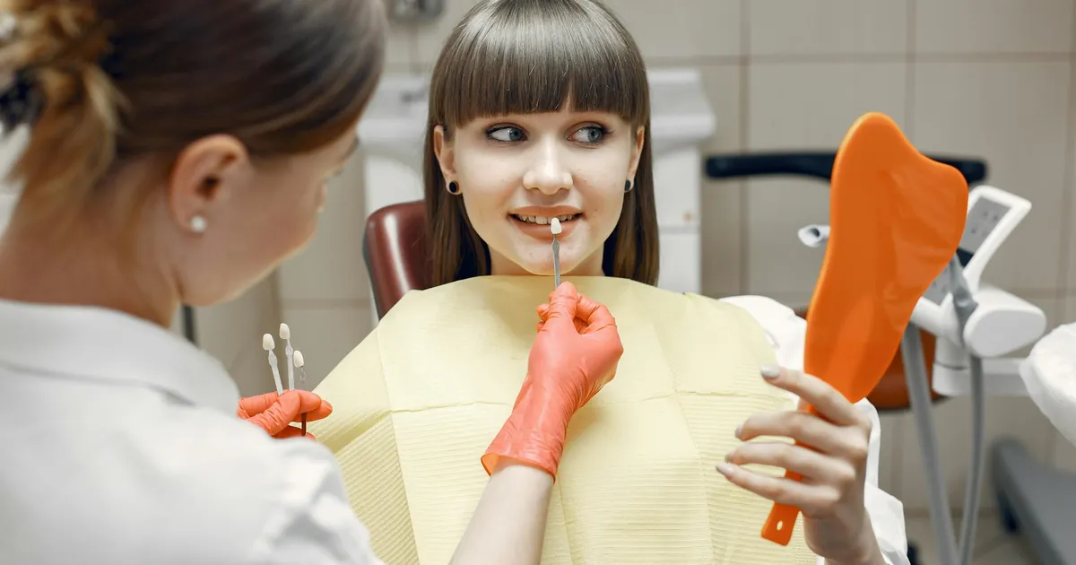 Dentist consults a young woman on veneers using dental tools and mirror in a clinic.