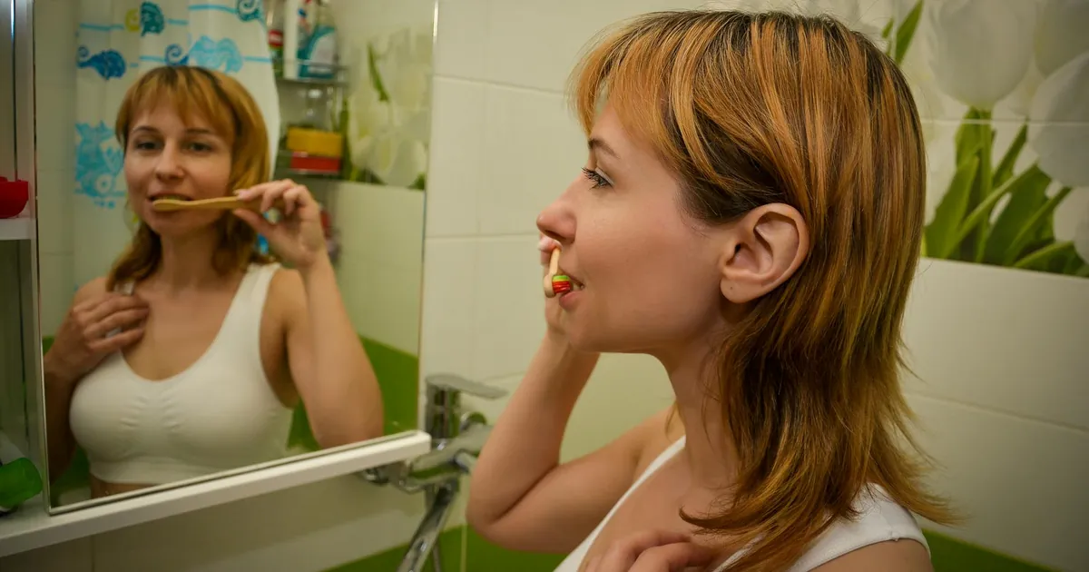 Redhead woman brushes teeth in bright bathroom, focusing on dental hygiene.