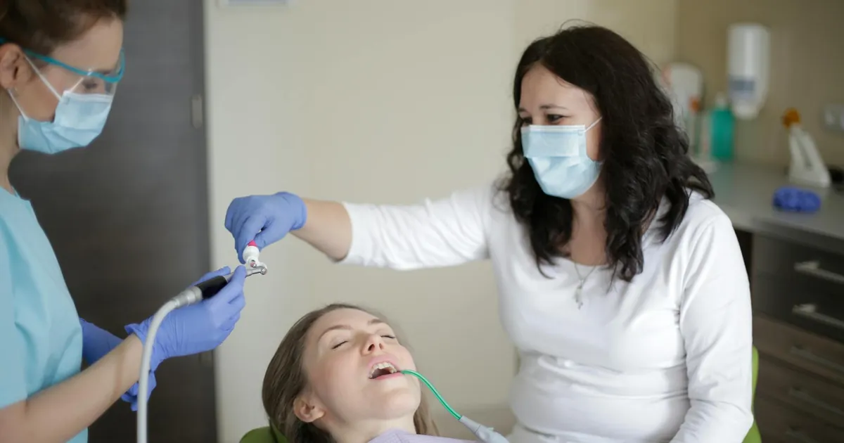 Middle aged female lying in dental chair with tube suction in mouth while getting professional treatment to fill cavity in tooth in dental clinic