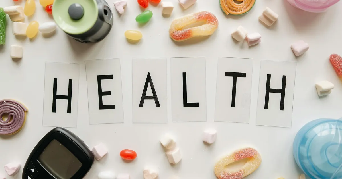 Creative flat lay with sweets around a 'HEALTH' text and monitoring device, symbolizing diabetes awareness.