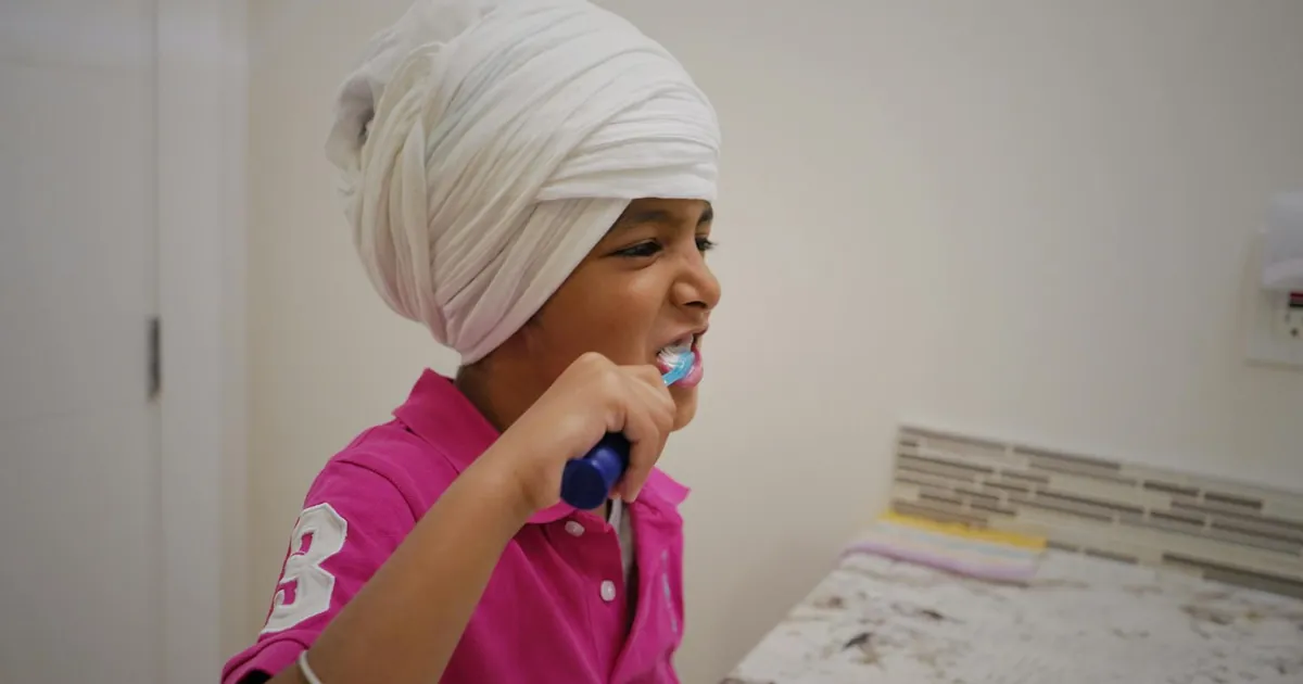 Young child in a turban practicing good dental hygiene by brushing teeth indoors.