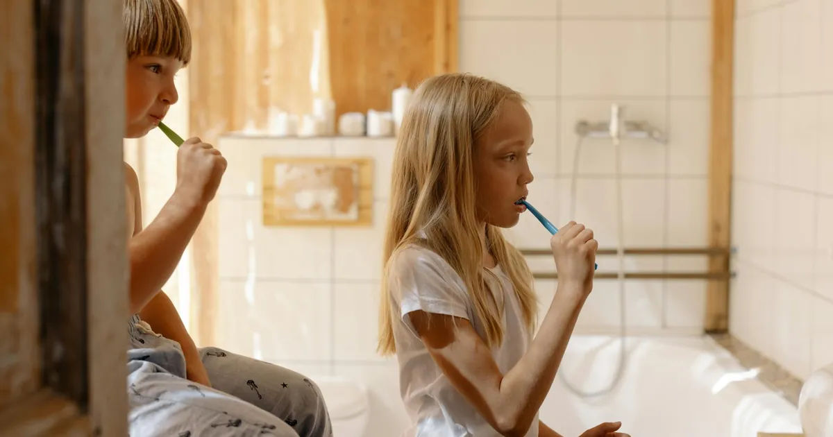 Two children brushing teeth together in a sunlit bathroom, emphasizing oral care.