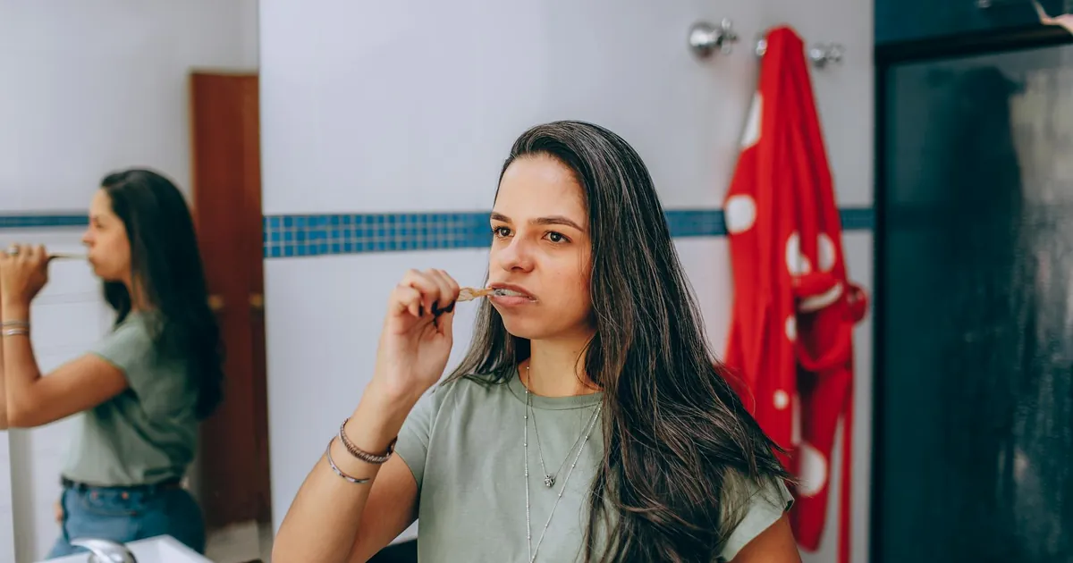 Young woman brushing teeth in a modern bathroom with a red towel hanging nearby.