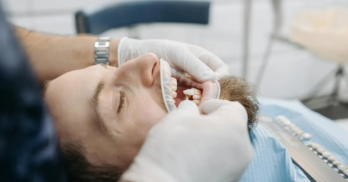 Dentist using shade guide to match patient's teeth color in dental clinic.