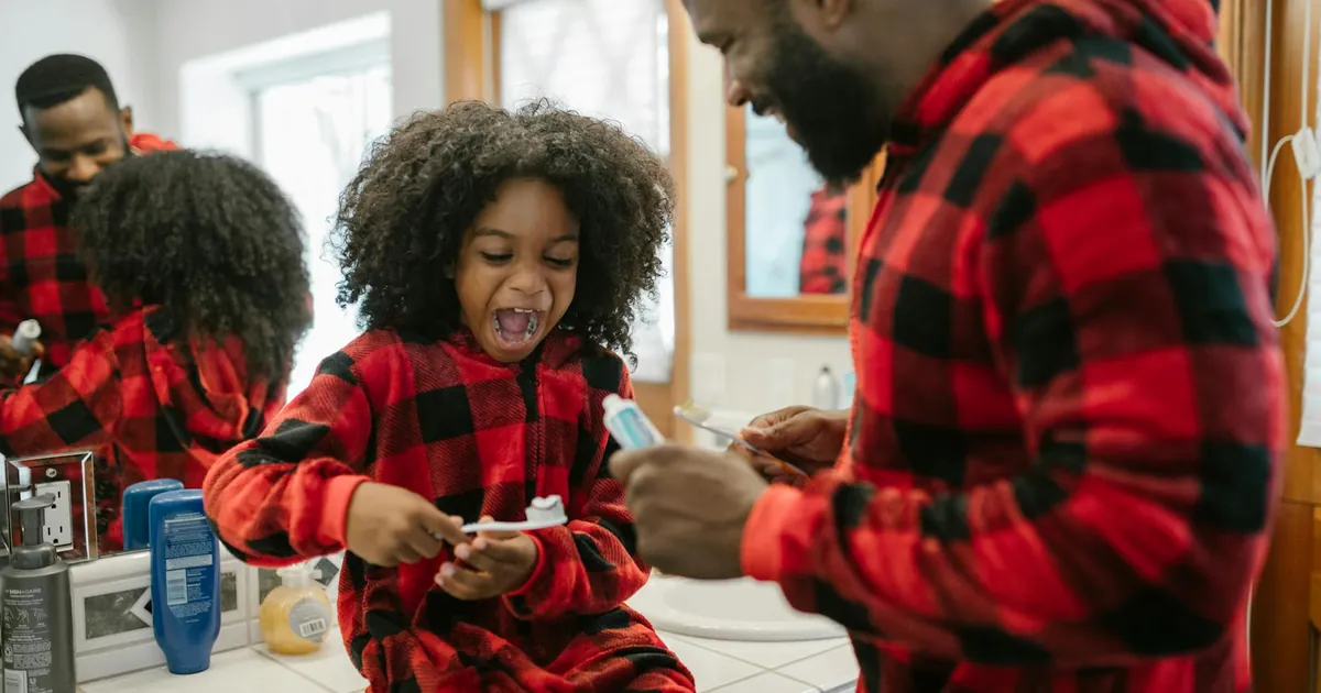A happy father and daughter in matching pajamas brushing teeth in a bright bathroom.