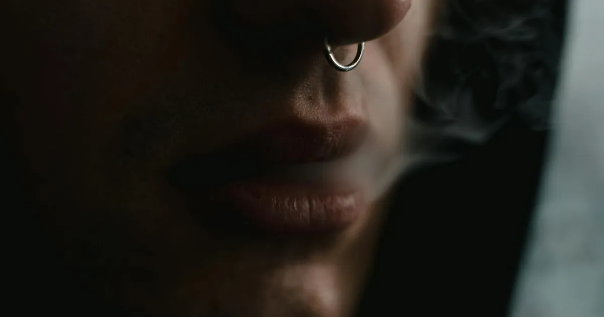 Close-up moody portrait highlighting a nose ring and smoke, exploring habit themes.