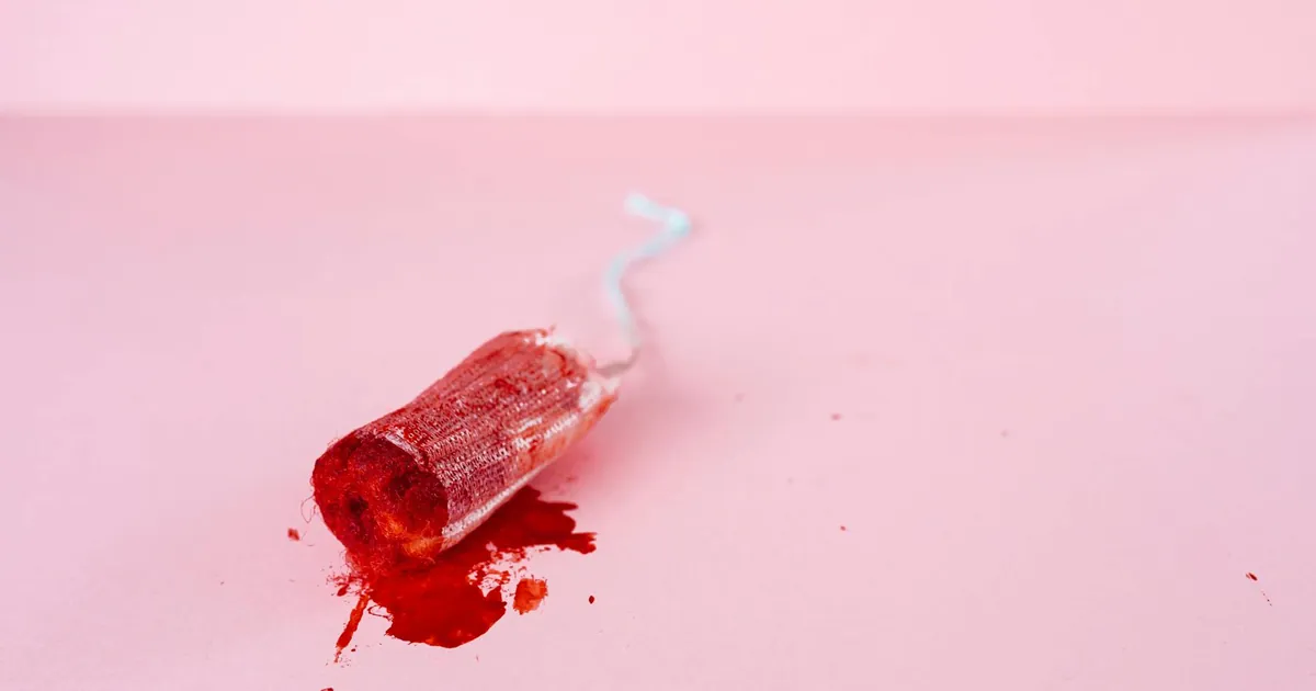 A used tampon on a pink surface, highlighting menstrual themes and women's health awareness.