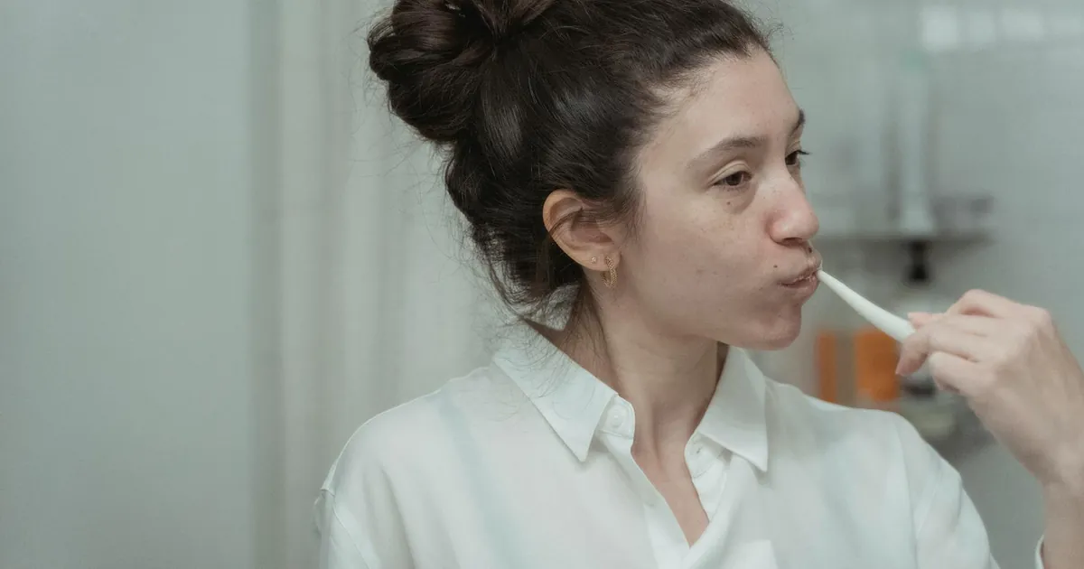 A woman brushes her teeth in the bathroom as part of her daily oral hygiene routine.