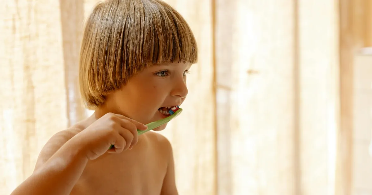 Young boy brushing teeth indoors in soft natural light, promoting dental care routines.