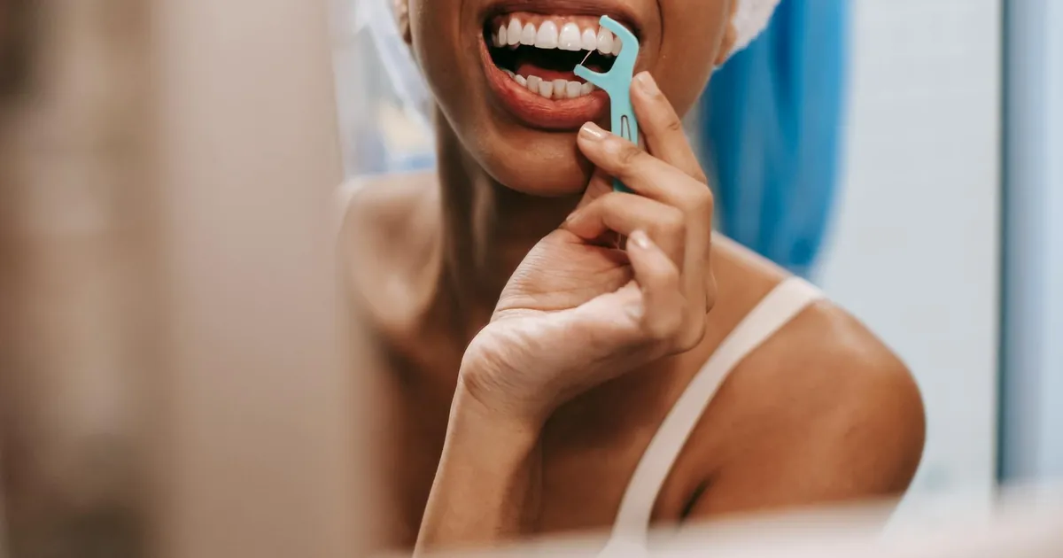 Young African American woman practicing oral hygiene by flossing teeth in front of a bathroom mirror.