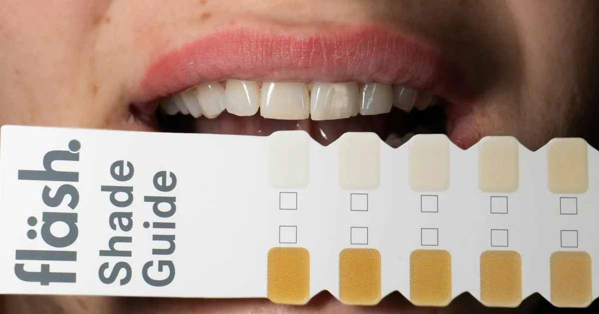 Adult holding a dental shade guide to compare tooth whitening results.