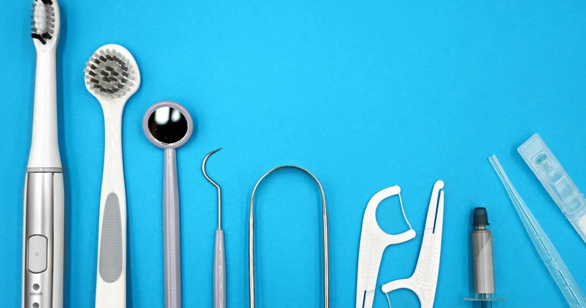 Flat lay of dental care tools including toothbrushes, dental mirror, and floss sticks on blue background.