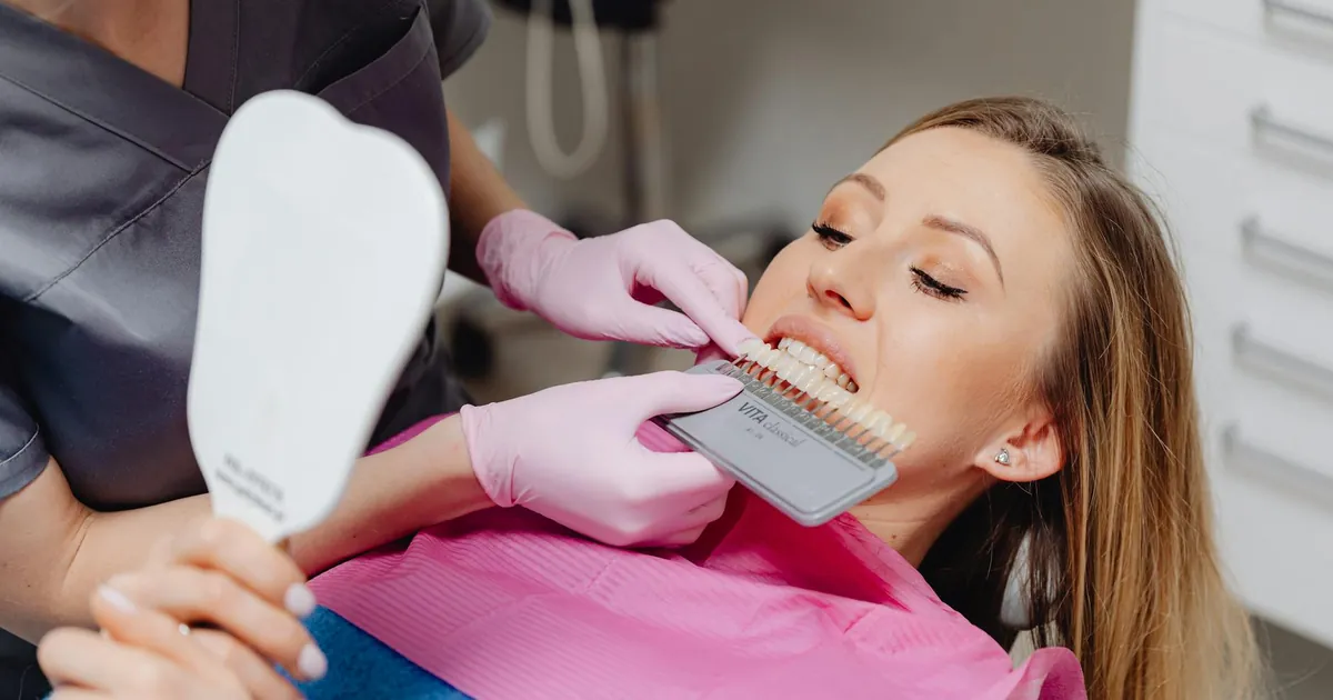 Dentist using a shade guide to match tooth color for a patient in a dental clinic.
