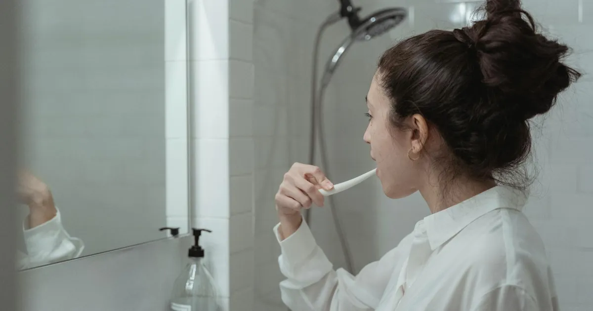 Woman brushing teeth in a modern bathroom, promoting daily oral health habits.