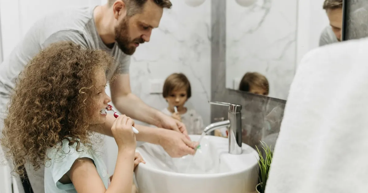 Father and children enjoying morning dental routine by brushing teeth together in elegant bathroom.
