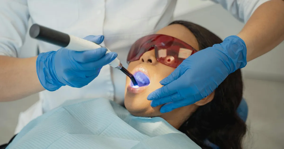 Dentist performing dental treatment using curing light on patient wearing protective eyewear.