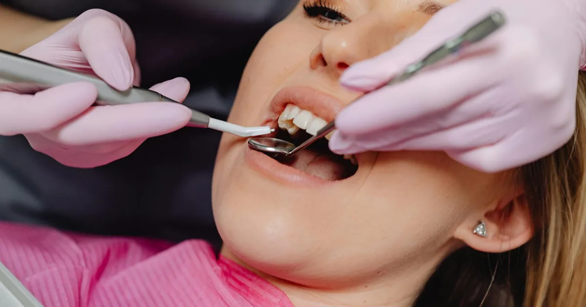 Close-up of a woman receiving dental care with a dentist using tools inside a clinic.